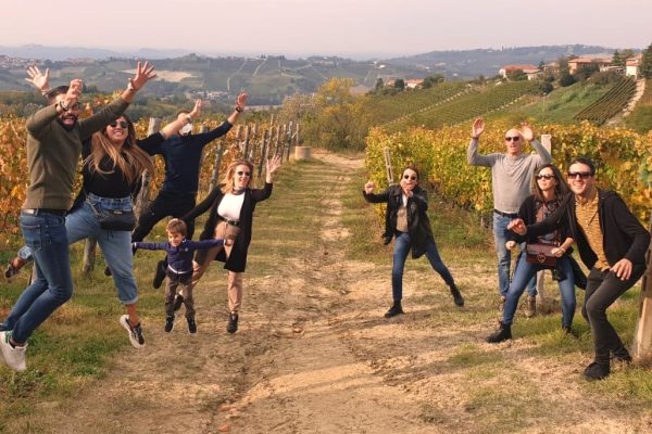 Un gruppo di ragazzi e ragazze saltano felici in mezzo ad una vigna